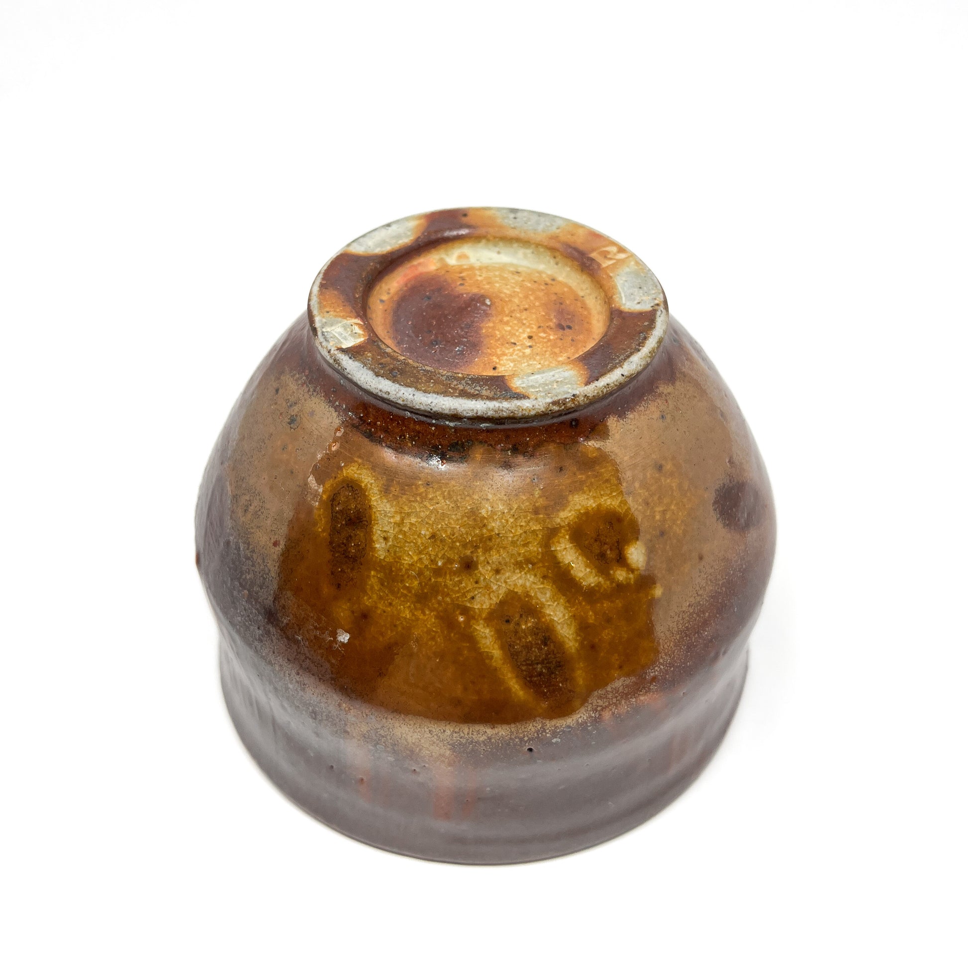 Bottom view of a rustic, dark glazed tea bowl showing the unglazed foot and textured surface.
