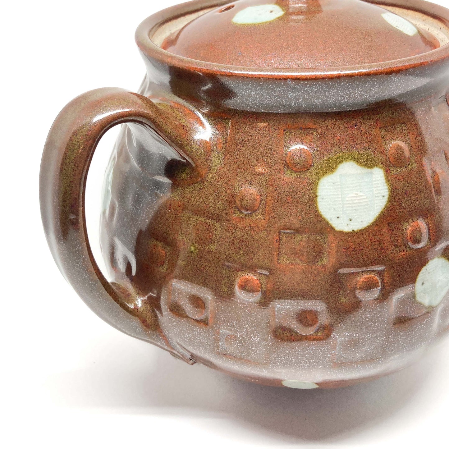 Detailed view of a brown ceramic teapot handle and body with raised geometric patterns and light-colored polka dots.