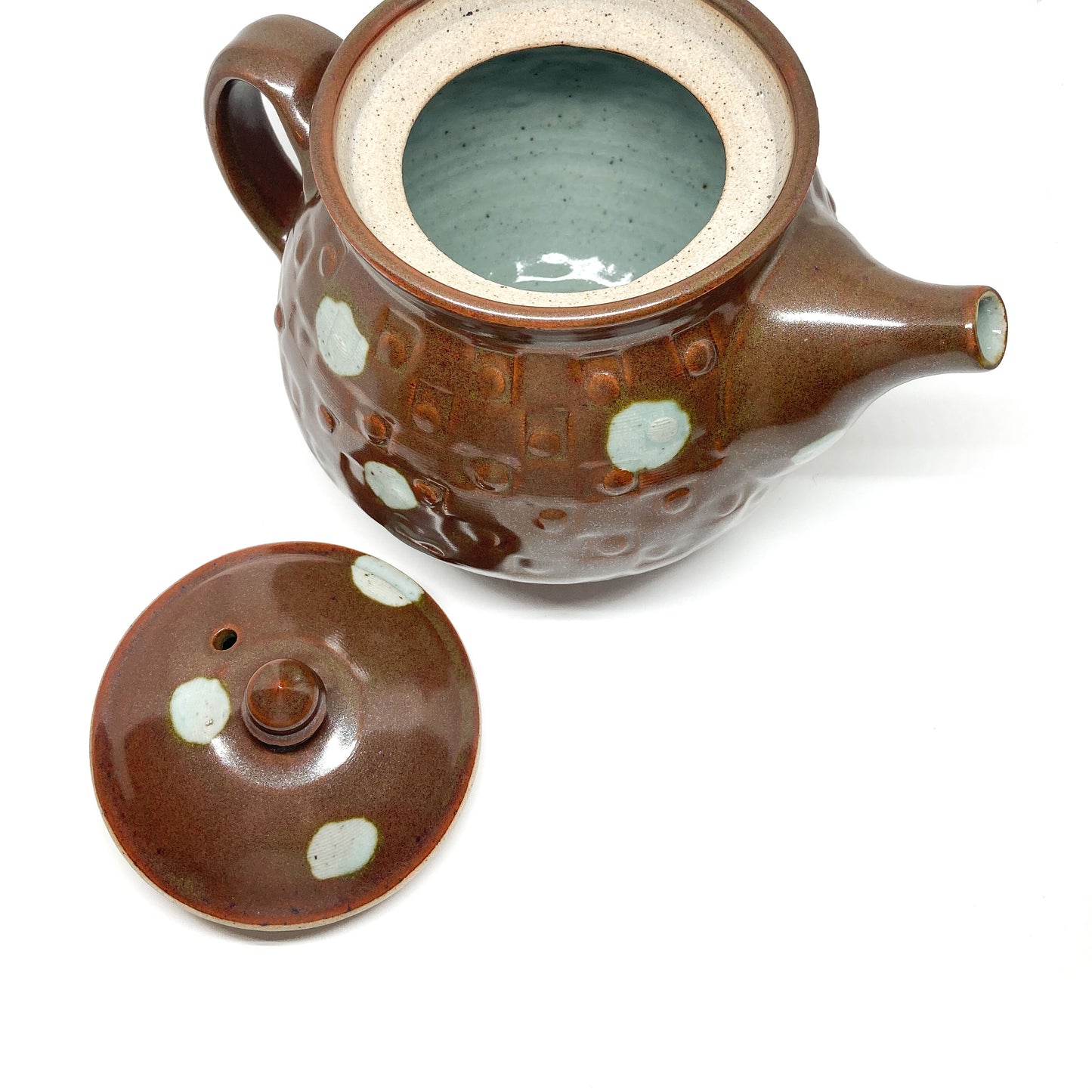 Open brown polka dot teapot with a detached lid revealing a light blue interior. Handle and spout are visible.