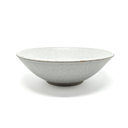 A speckled light-toned ceramic bowl with subtle vertical ridges and a visible unglazed base.