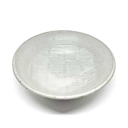 Top-down view of a shallow, speckled light ceramic bowl with subtle concentric rings on the interior.