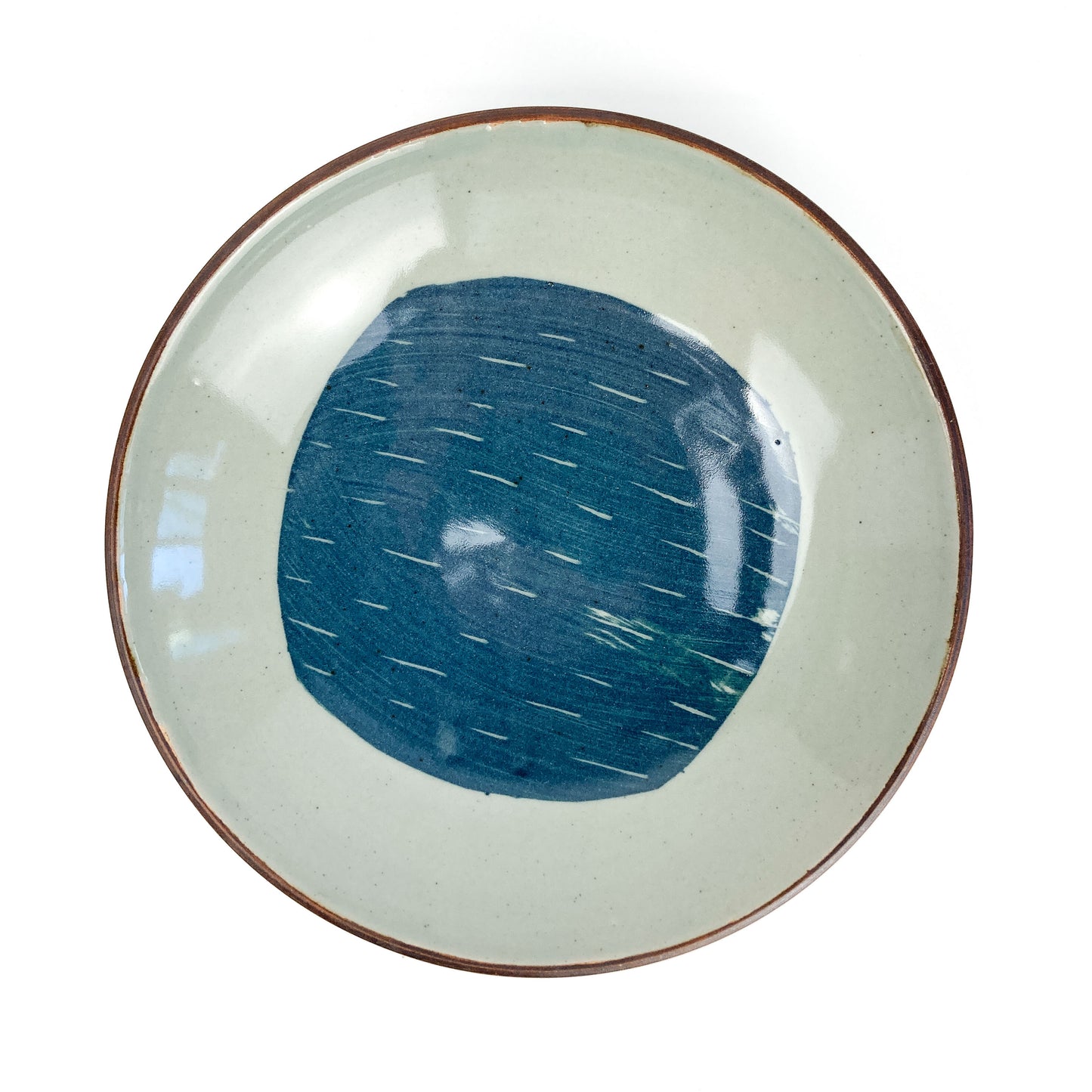 Overhead view of a round, light-toned ceramic plate with a dark rim and a central blue circular design with white dashes.