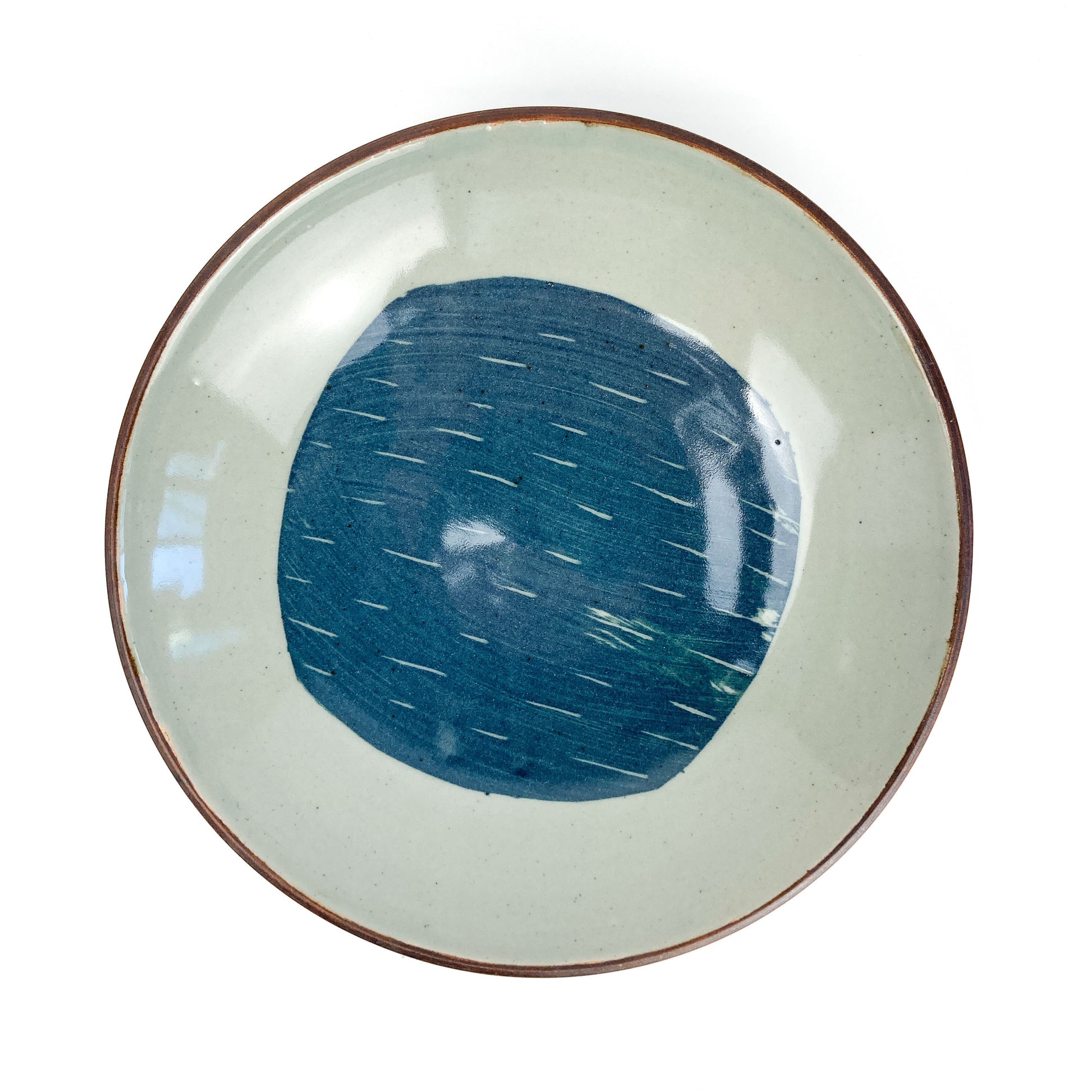 Overhead view of a round, light-toned ceramic plate with a dark rim and a central blue circular design with white dashes.