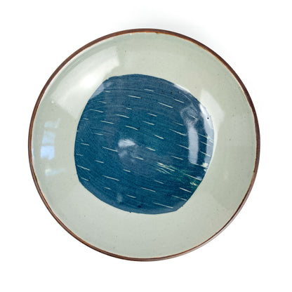 Overhead view of a round, light-toned ceramic plate with a dark rim and a central blue circular design with white dashes.