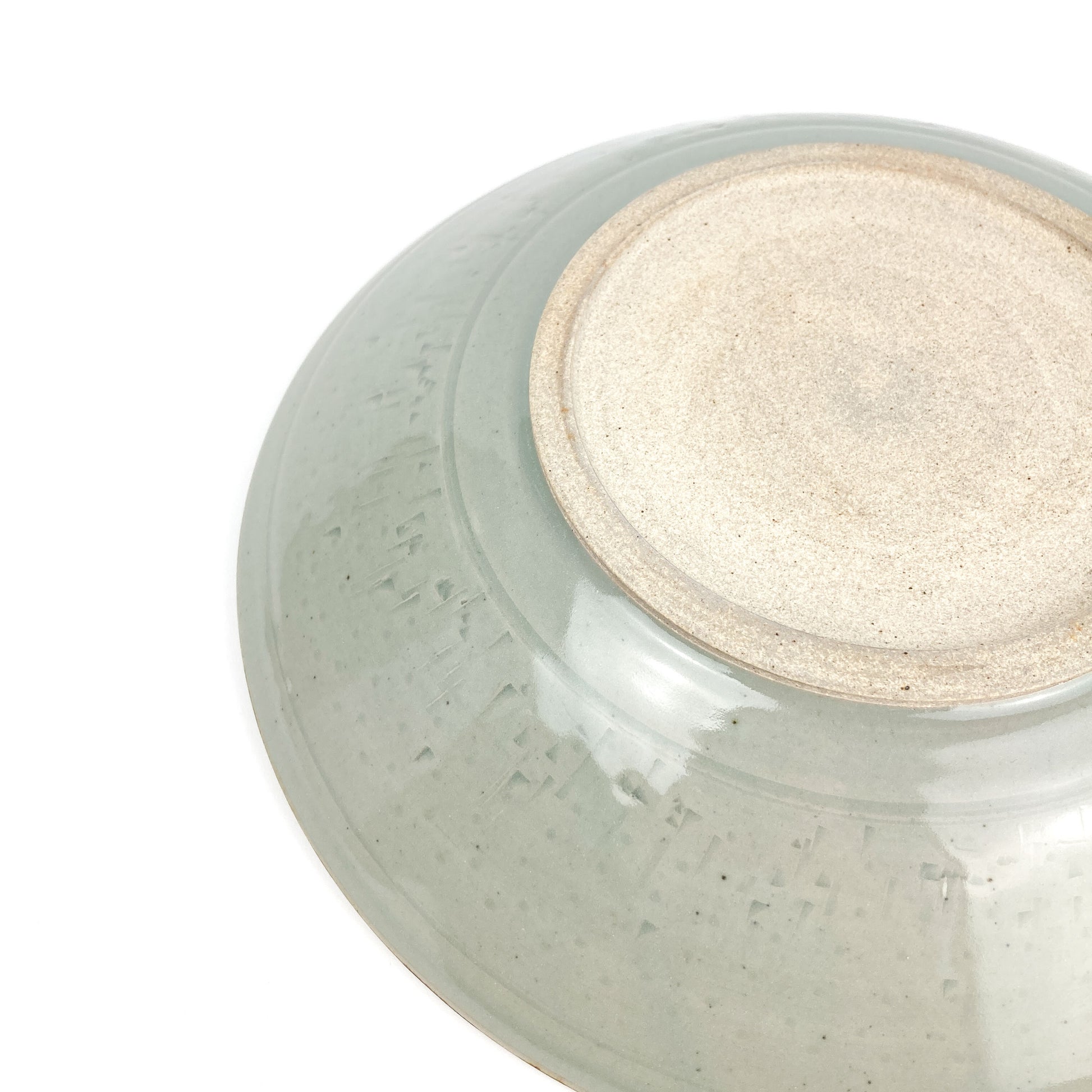 Bottom view of a light-glazed ceramic bowl showing the unglazed circular foot and subtle surface texture.