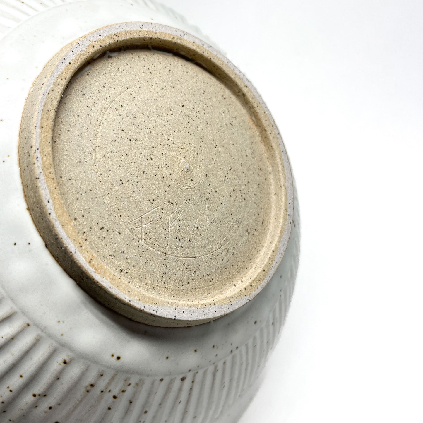 Underside of a speckled light ceramic bowl revealing an unglazed circular foot and faint etched markings.