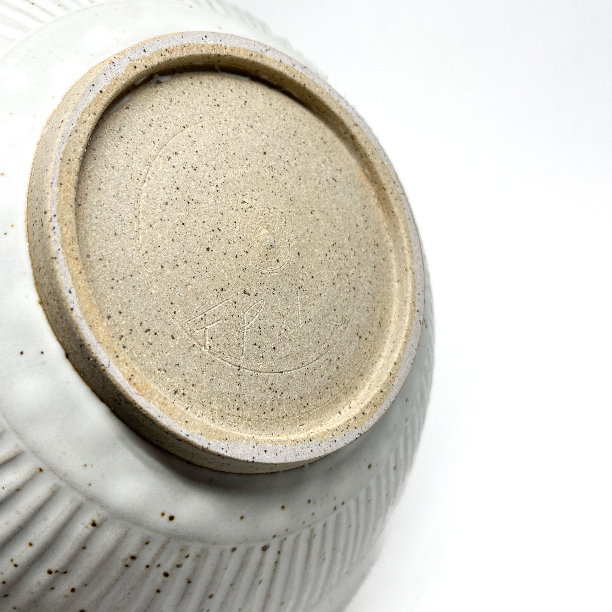 Underside of a speckled light ceramic bowl revealing an unglazed circular foot and faint etched markings.