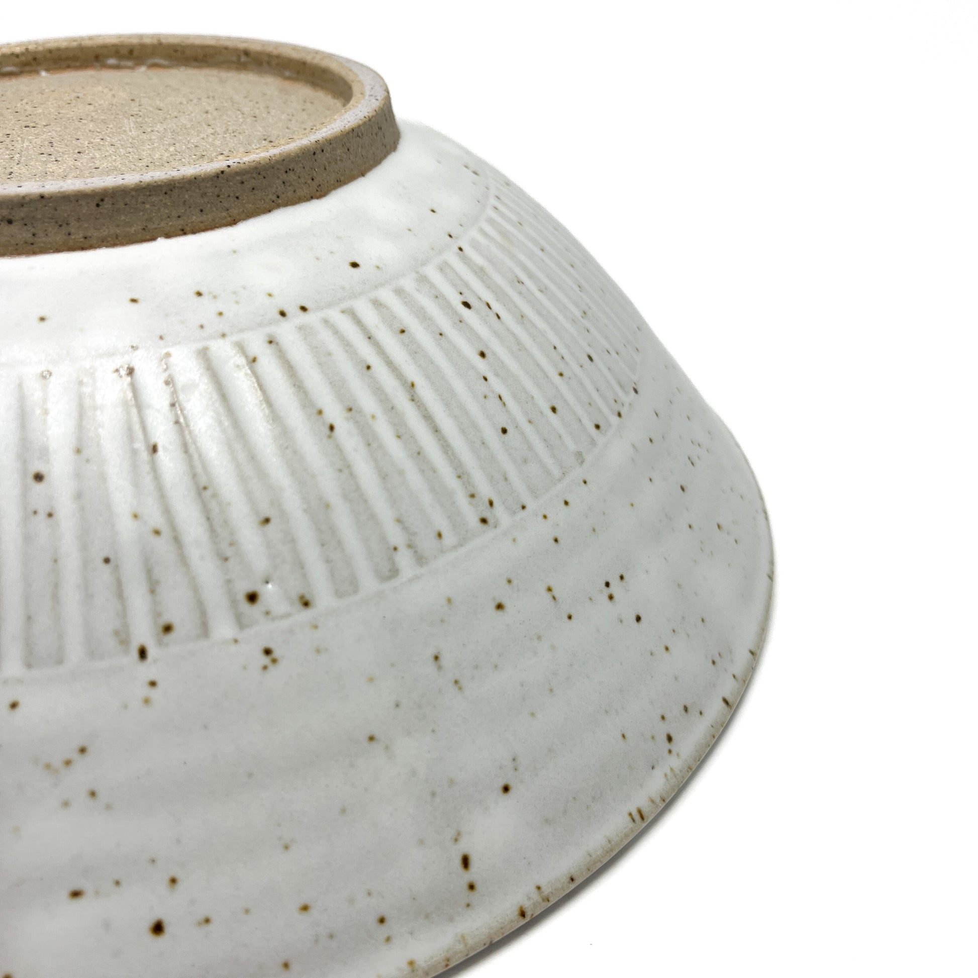 Side view of a speckled light ceramic bowl showing vertical ridges and an unglazed circular base.