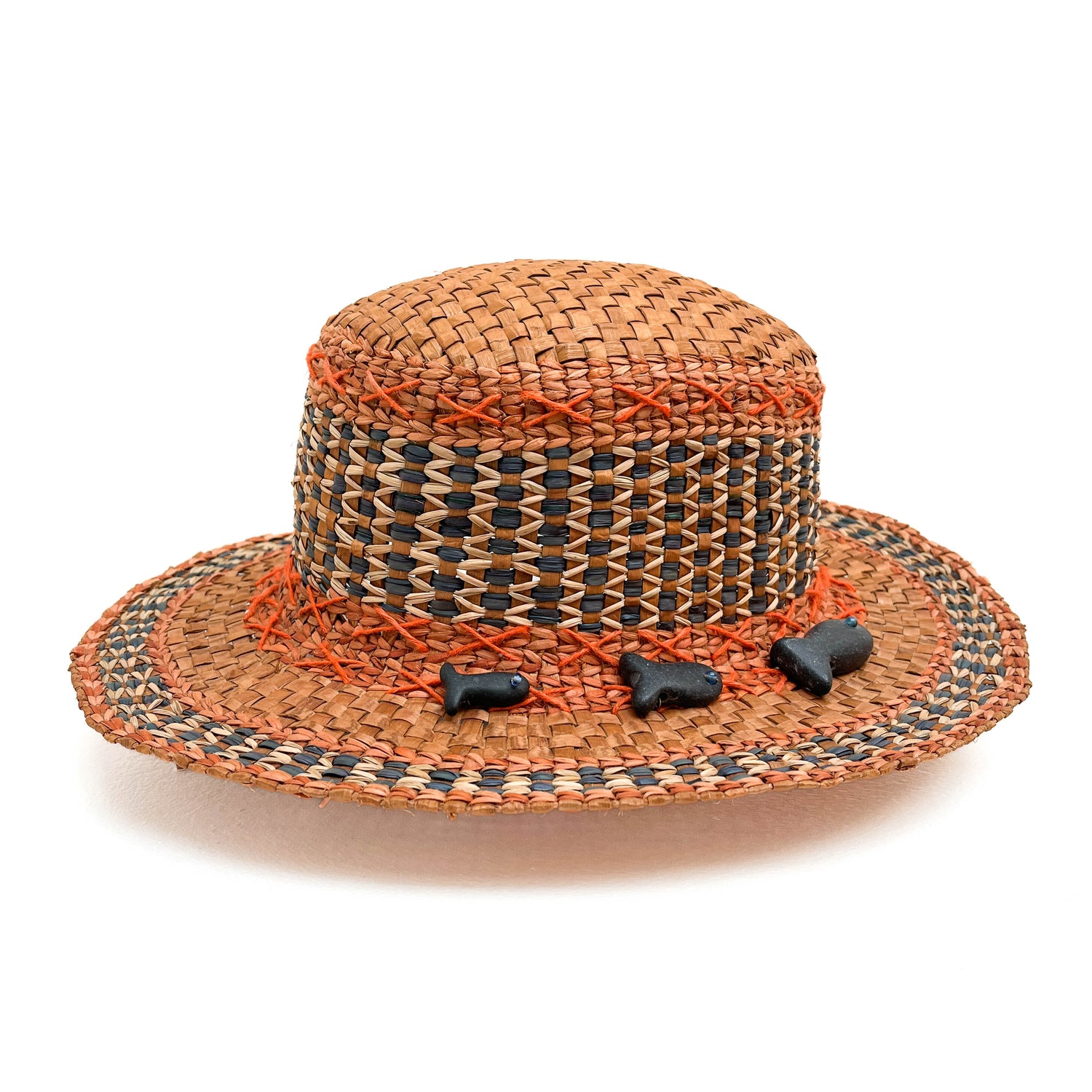 A woven hat with a cylindrical crown and wide brim, featuring geometric patterns and small, dark figurines.