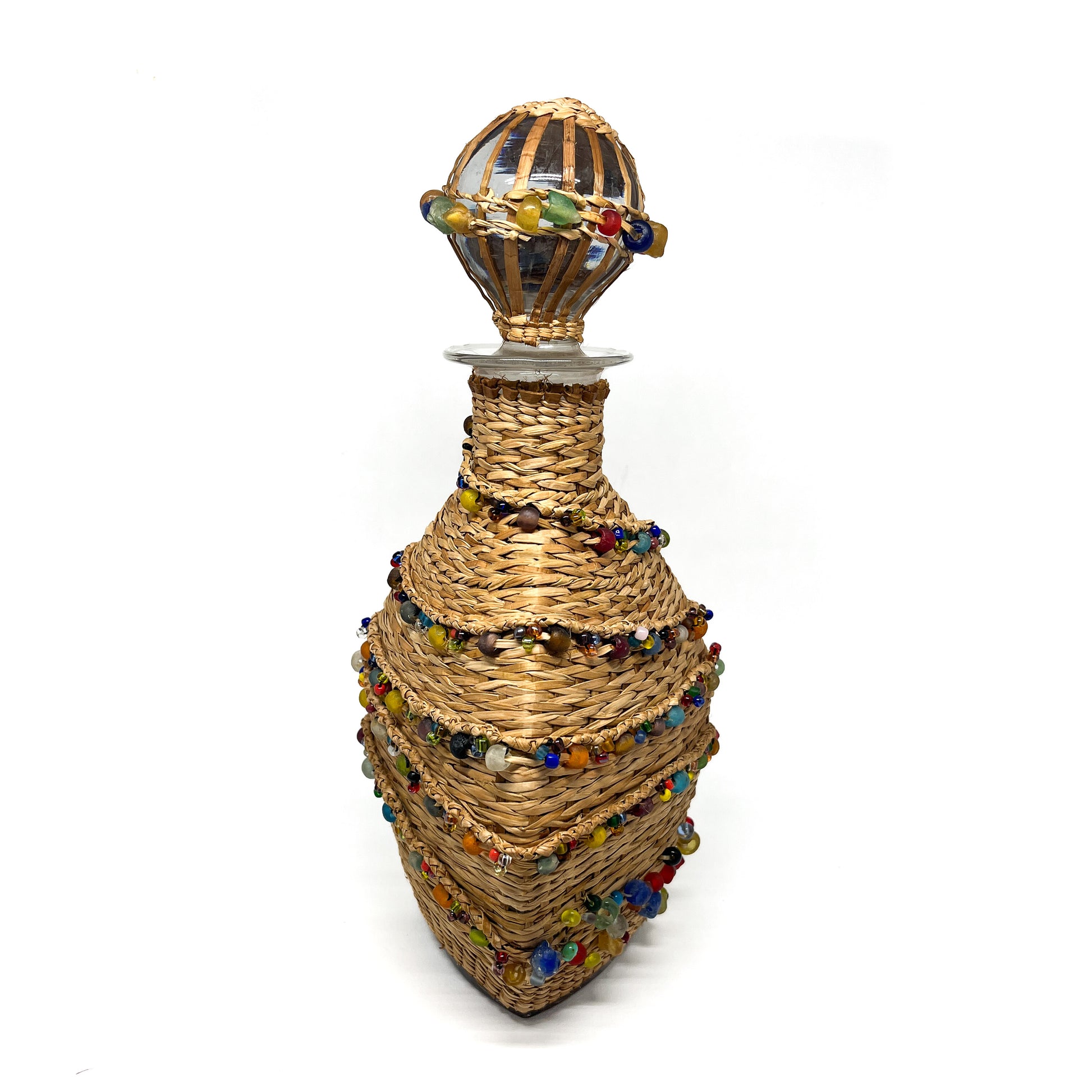 A decanter wrapped in woven material and adorned with colorful beads, with a glass stopper.