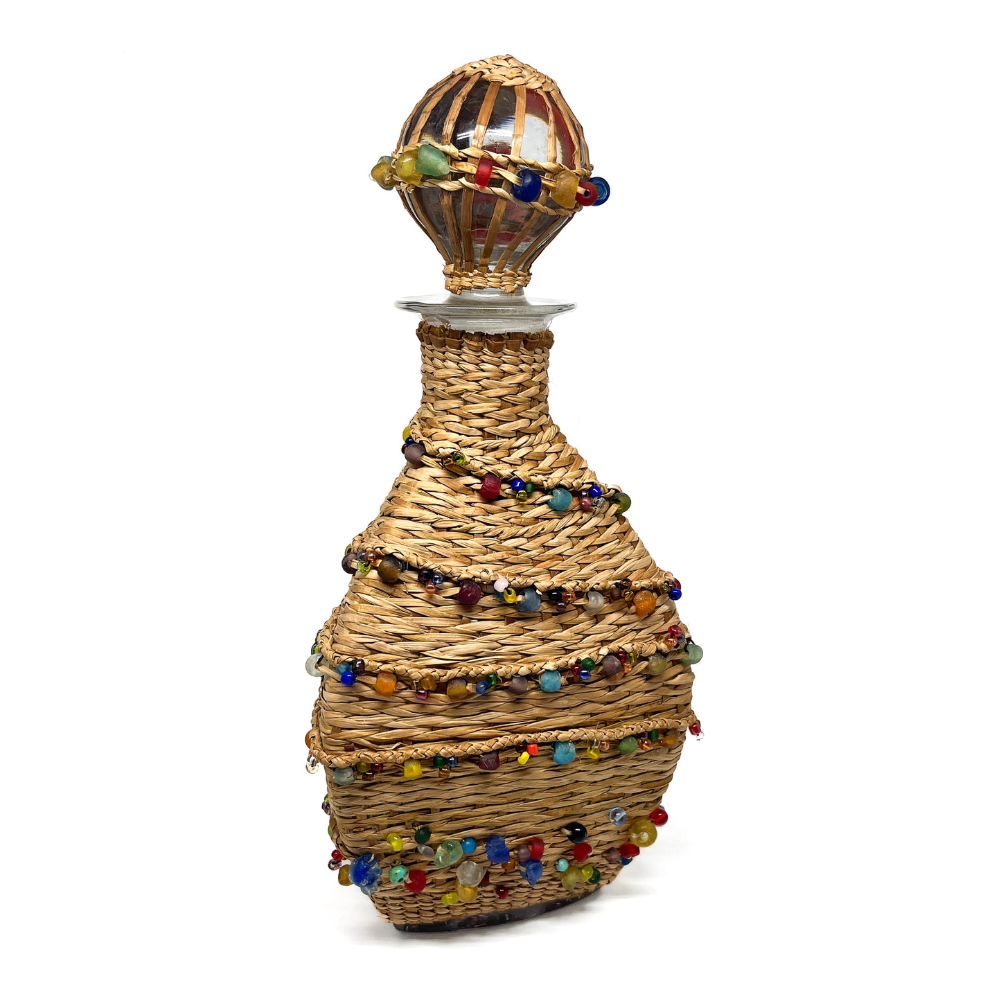 A decanter wrapped in woven material and adorned with colorful beads, with a glass stopper.