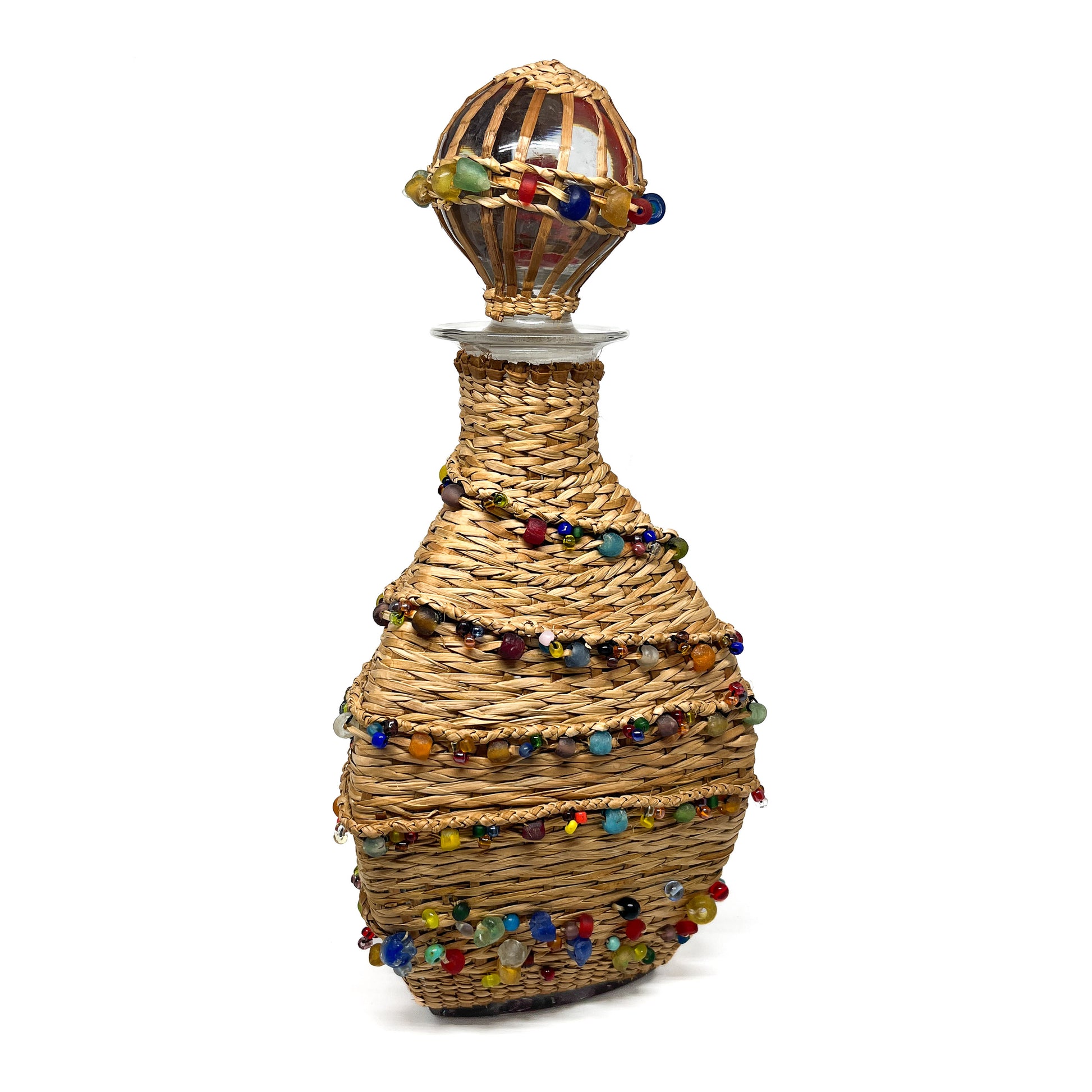 A decanter wrapped in woven material and adorned with colorful beads, with a glass stopper.