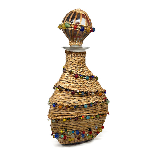 A decanter wrapped in woven material and adorned with colorful beads, with a glass stopper.