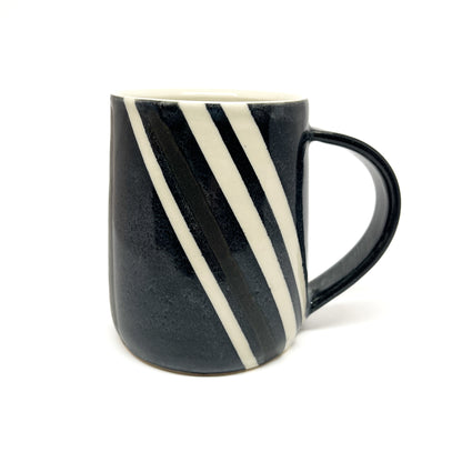 A ceramic striped mug with diagonal black and white bands and a black handle. The mug's interior is a light tone.