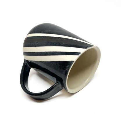 Angled view of a ceramic pottery mug with diagonal black and white stripes and a black handle, showing its light-toned interior.