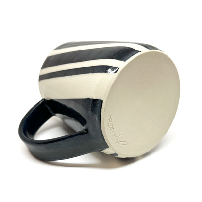 Bottom view of a ceramic pottery mug with diagonal black and white stripes and a black handle, showing a signature.