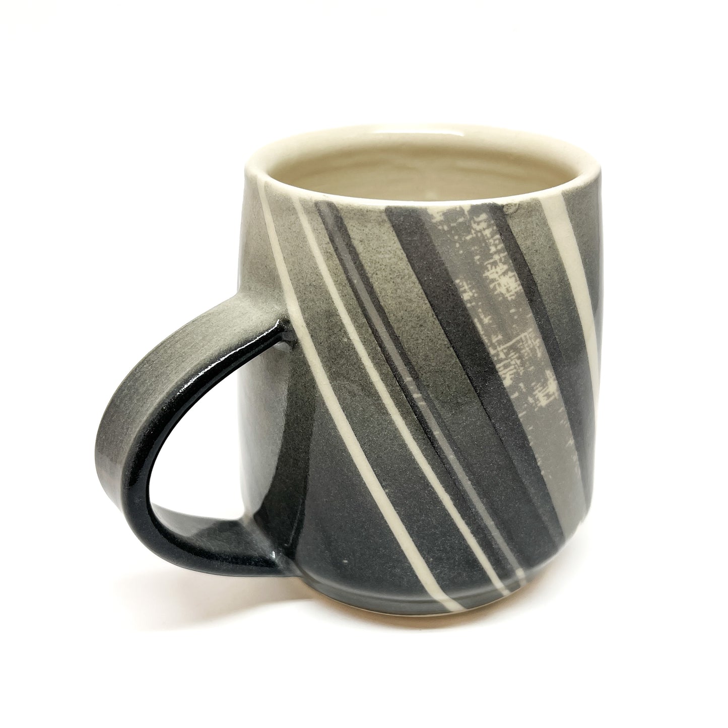 A wood-fired ceramic mug with diagonal stripes in shades of gray and white, and a dark handle. The mug's interior is a light color.