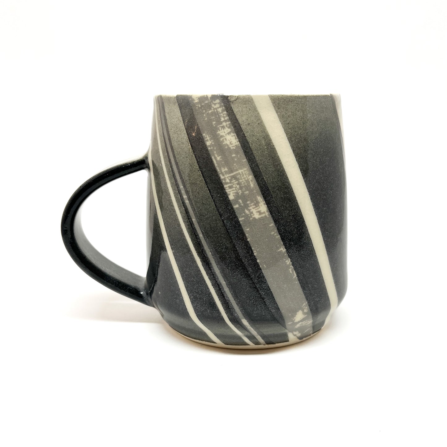 A Meta-Morphic Mug, a wood-fired ceramic mug with diagonal stripes in shades of gray and white, and a dark handle.