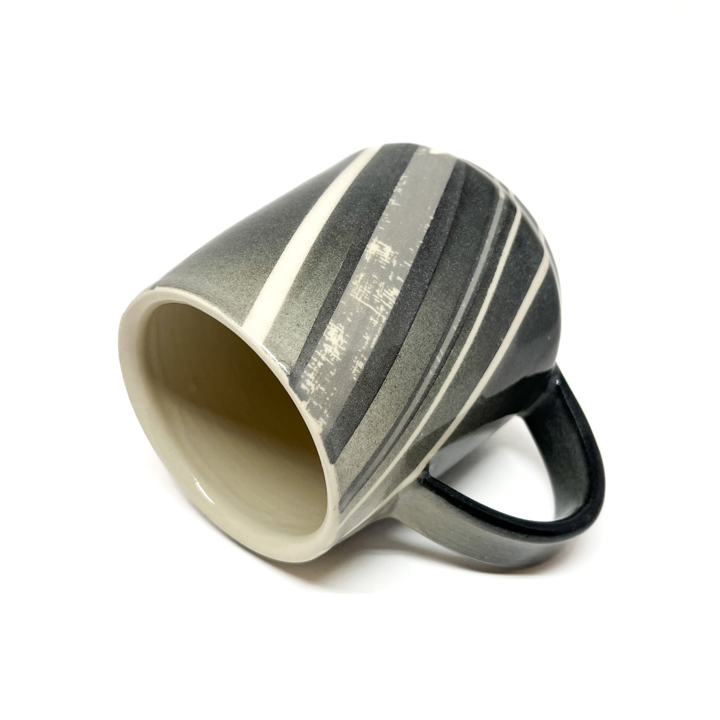 Striped ceramic mug with a handle, tilted on its side showing the interior.
