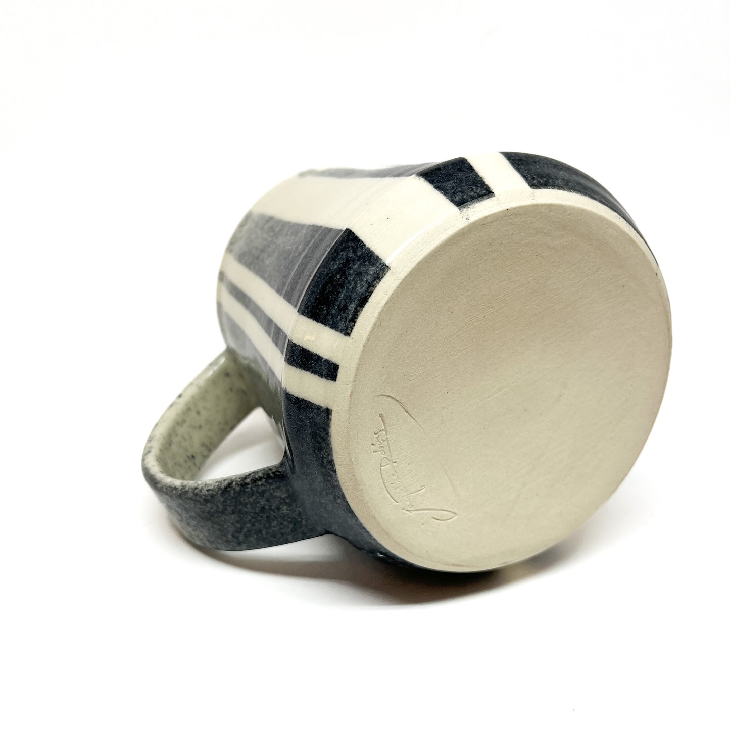 Striped ceramic mug with a handle, shown from the bottom, revealing a signature or mark.