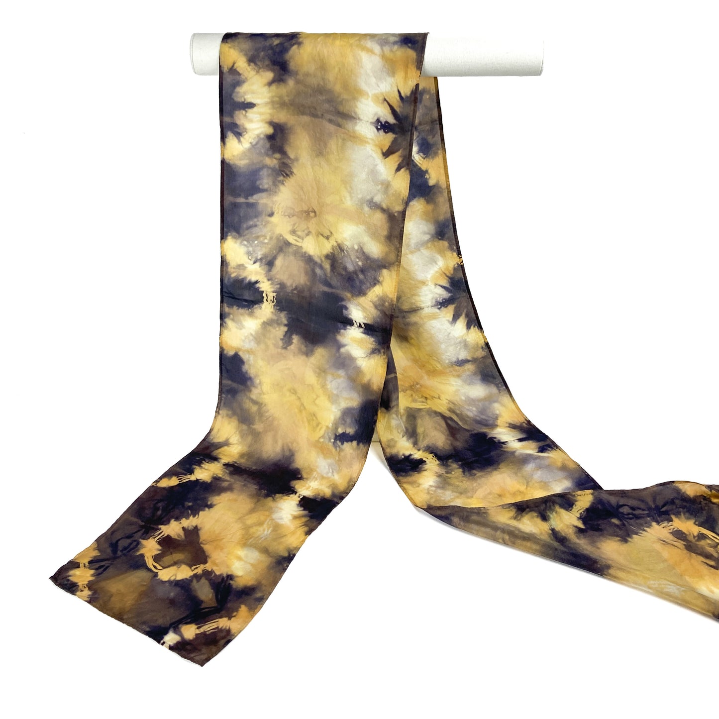 A Logwood and Myrobalan silk scarf with a starburst shibori tie-dye pattern hangs from a white cylindrical bar.