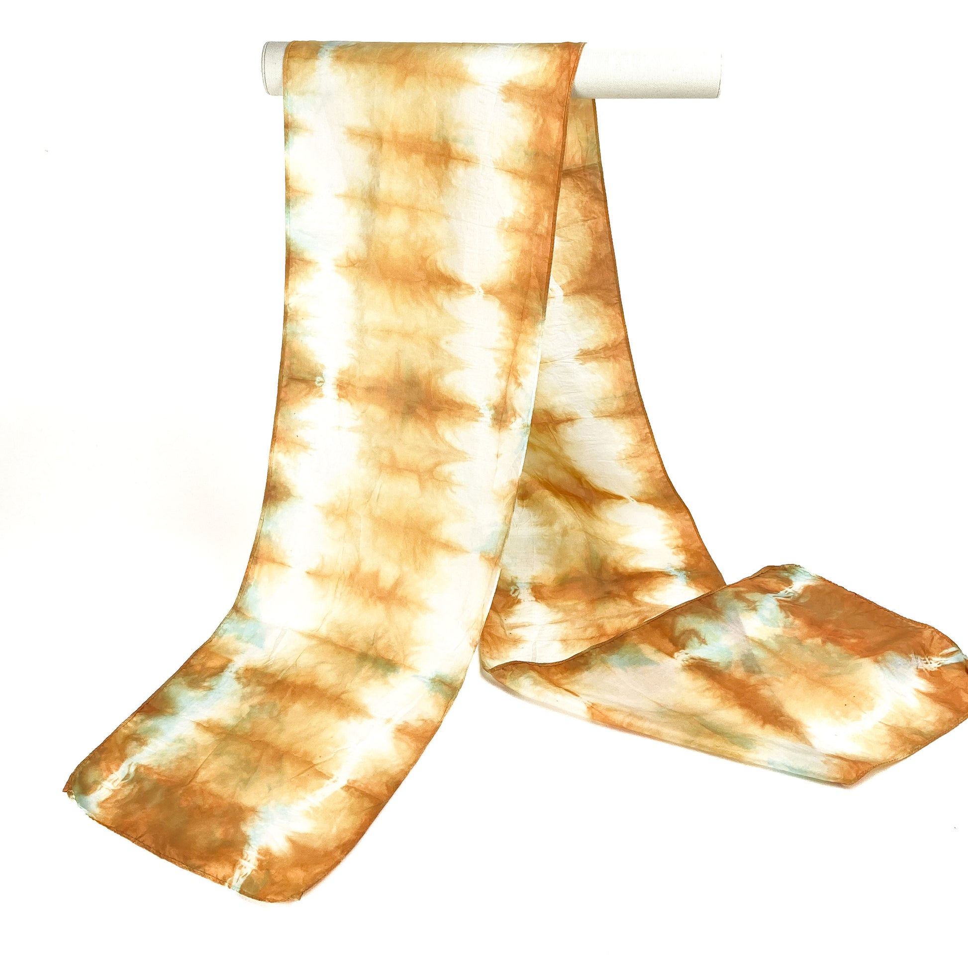 A Catechu silk scarf with a horizontally striped shibori tie-dye pattern drapes from a white cylindrical bar.