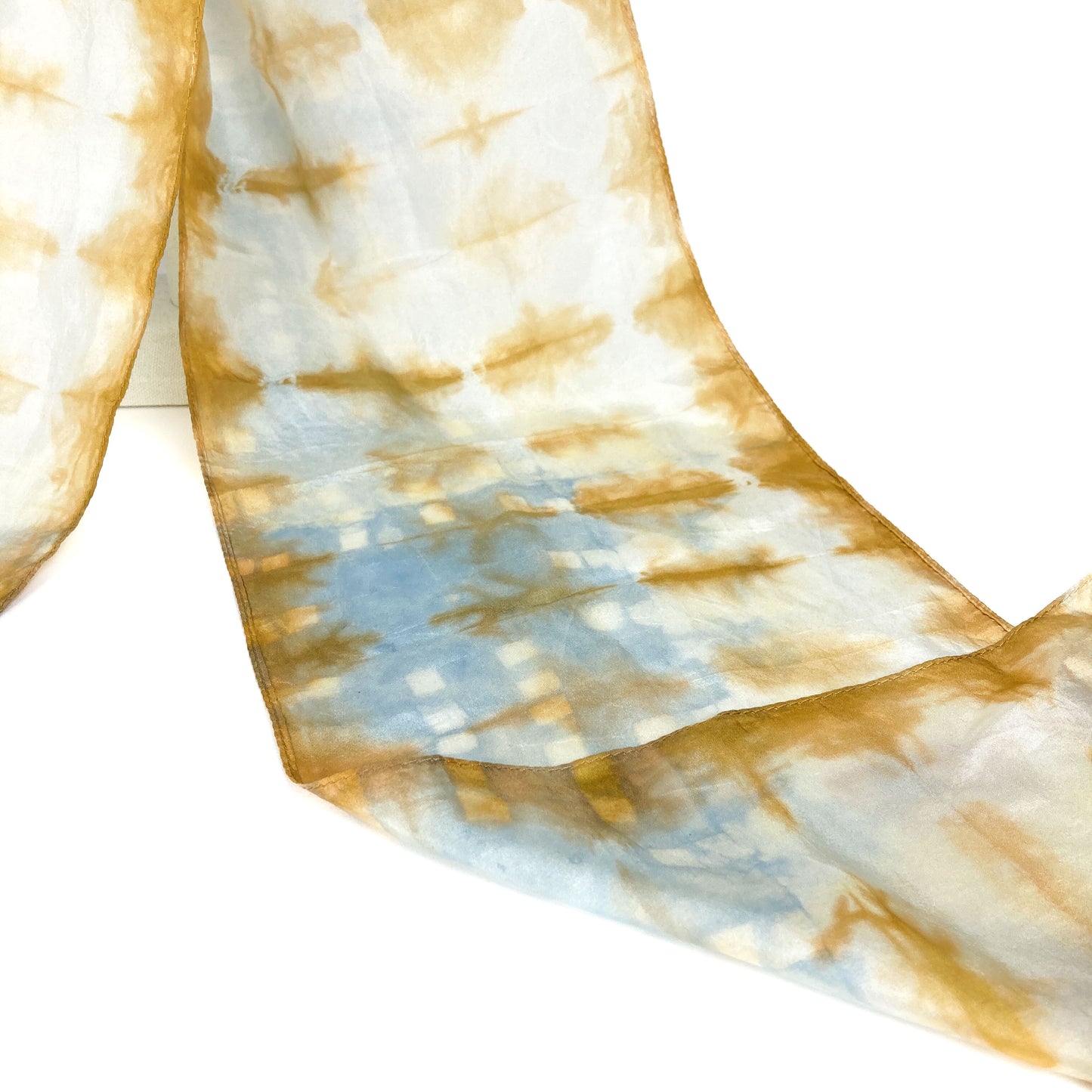 A section of a cutch tree bark silk scarf reveals its delicate, horizontally patterned shibori tie-dye.