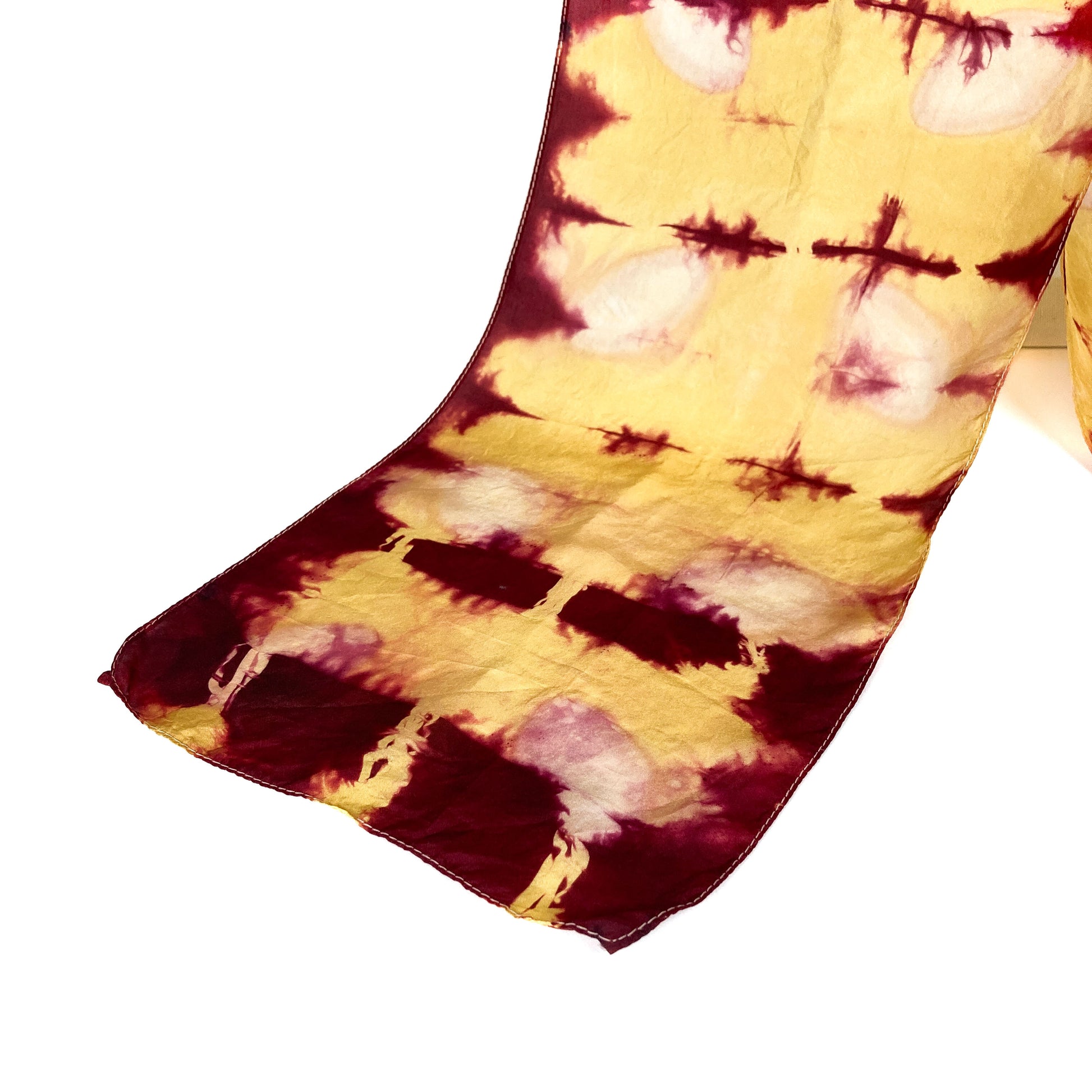 A section of a Rhubarb Lac silk scarf showcases its unique shibori tie-dye pattern with rich, blended hues.