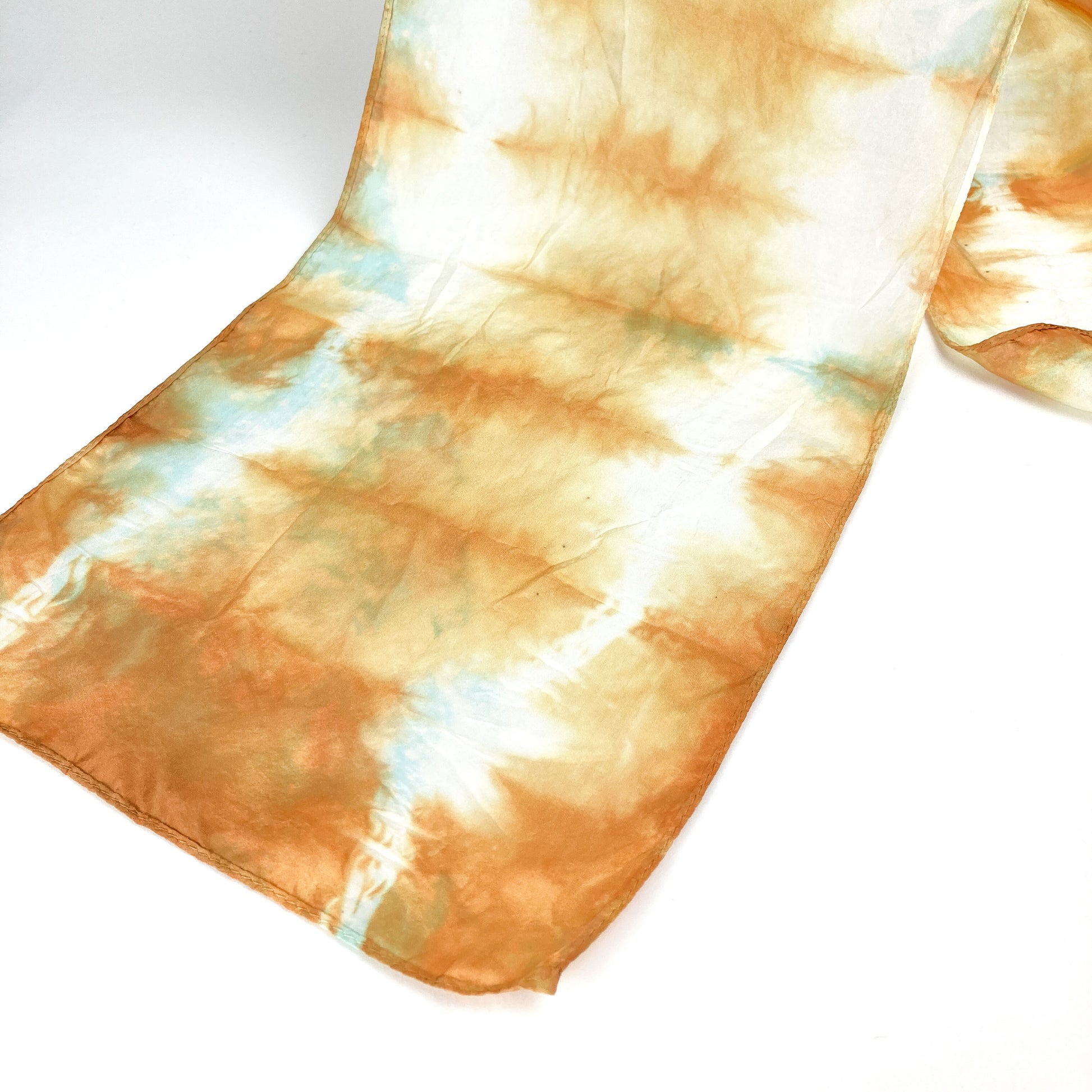 A section of a Catechu silk scarf displays its soft, horizontally blended shibori tie-dye design.