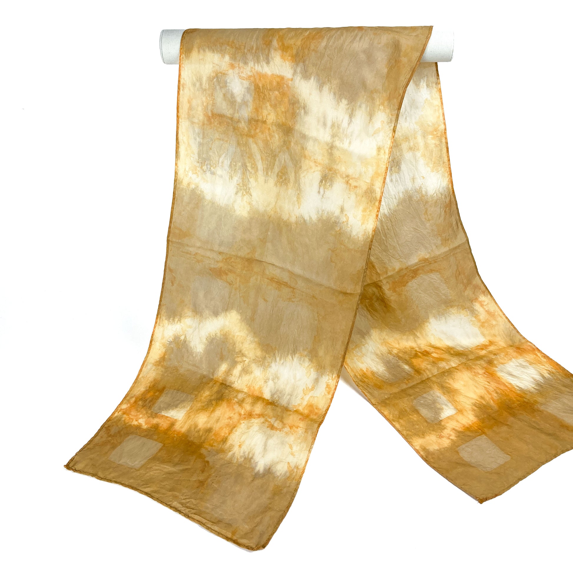 A Madder Root silk scarf with a soft, blended shibori tie-dye design hangs from a white cylindrical bar.