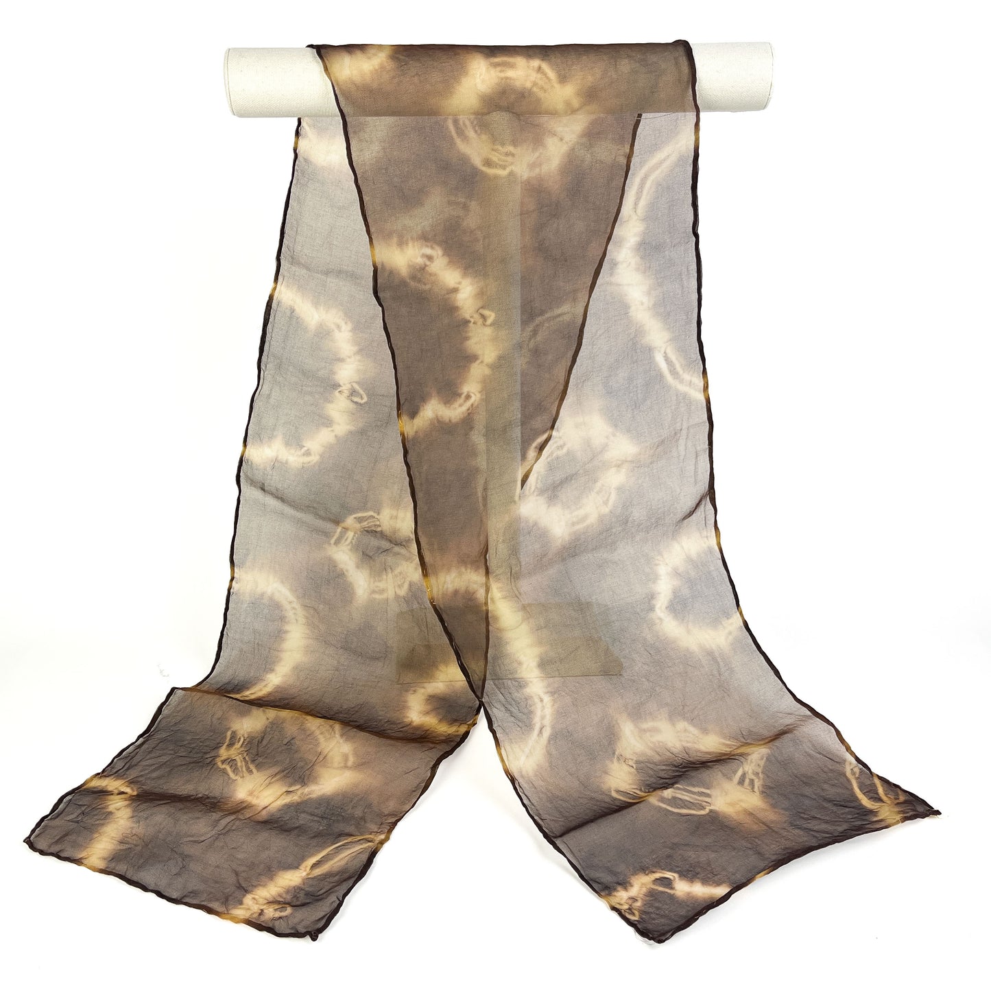 A Myrobalan silk scarf with a swirling resist shibori pattern hangs softly from a white cylindrical bar.