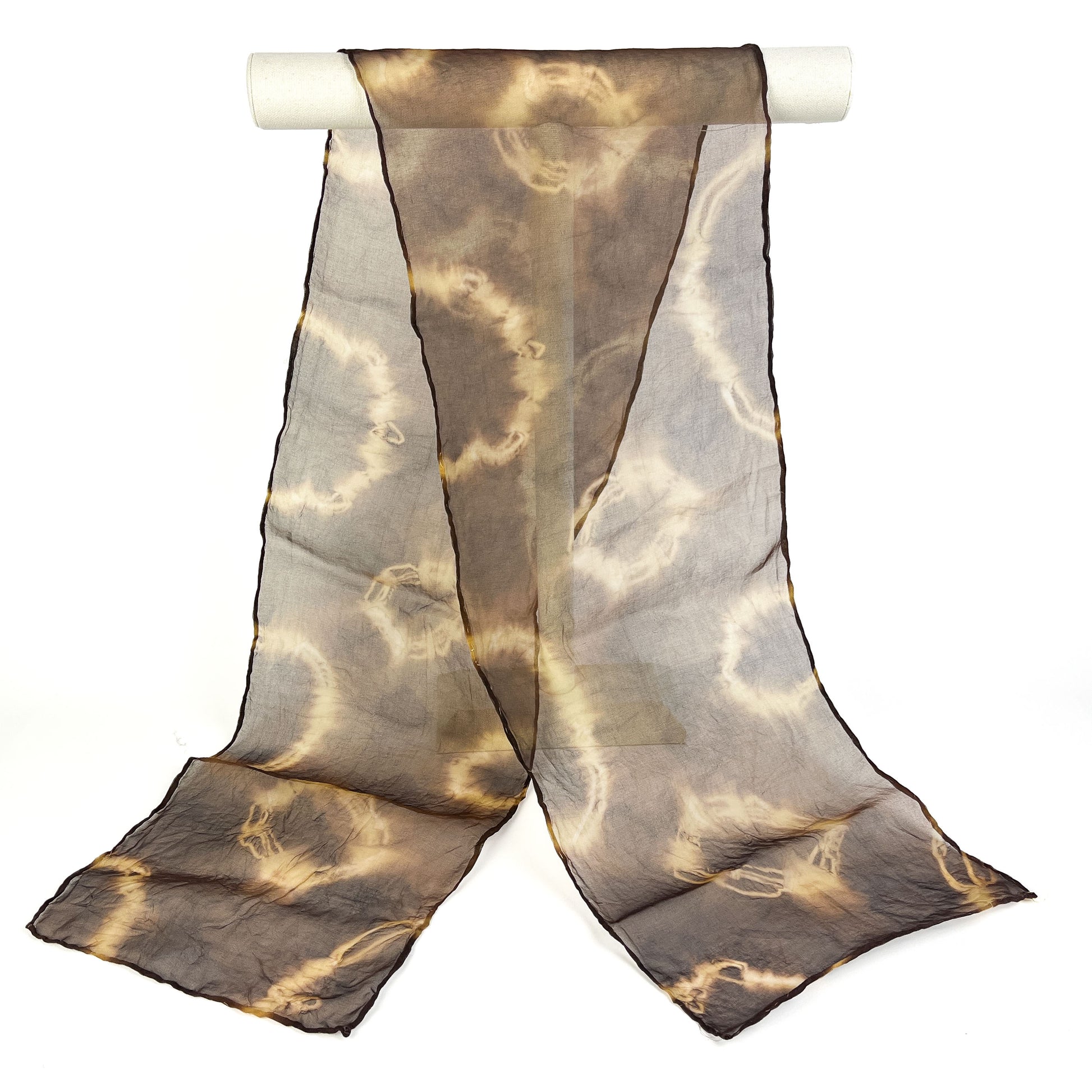 A Myrobalan silk scarf with a swirling resist shibori pattern hangs softly from a white cylindrical bar.