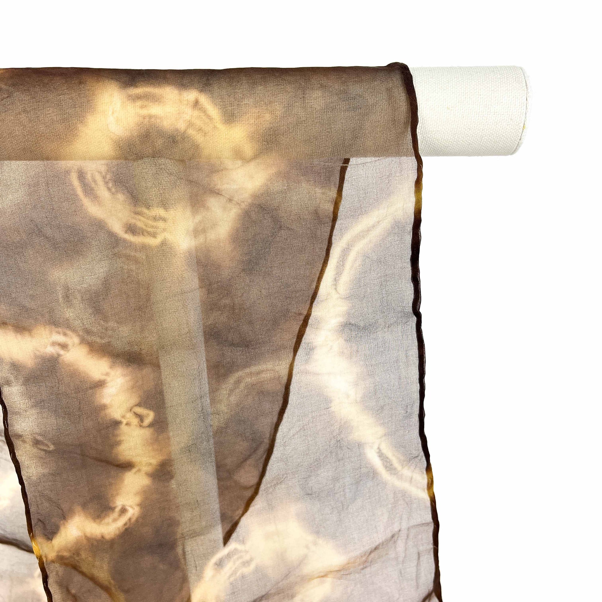 A close-up shows the sheer fabric and swirling resist shibori pattern of a Myrobalan silk scarf draped over a white bar.