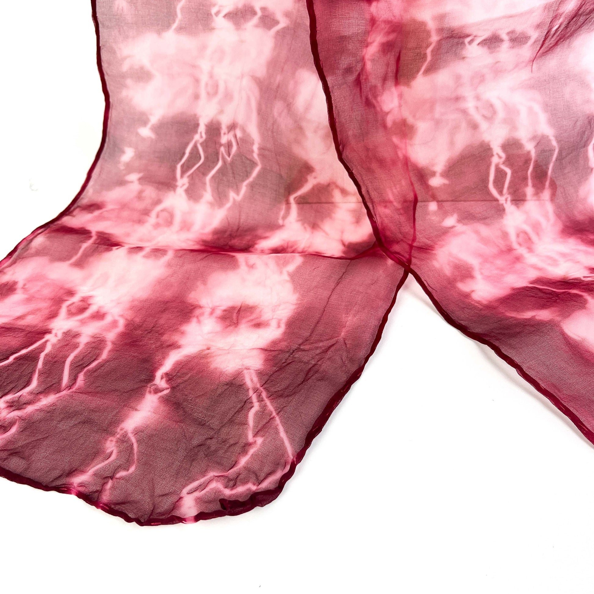 A close-up reveals the delicate texture and crackled shibori pattern of a pink hand-painted pure silk scarf.