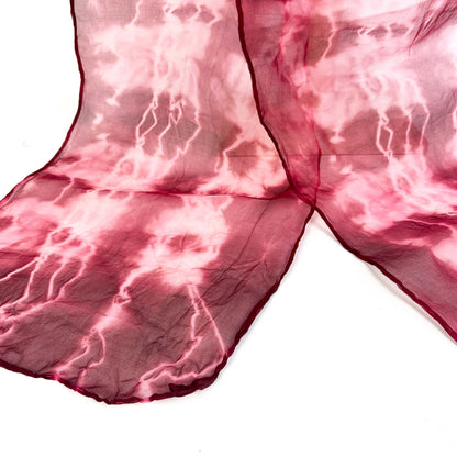 A close-up reveals the delicate texture and crackled shibori pattern of a pink hand-painted pure silk scarf.