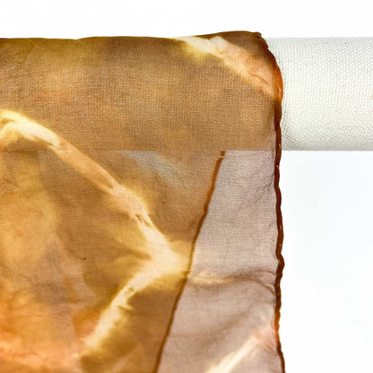 A close-up shows the delicate weave and circular resist shibori pattern of a Tea silk scarf draped over a white bar.