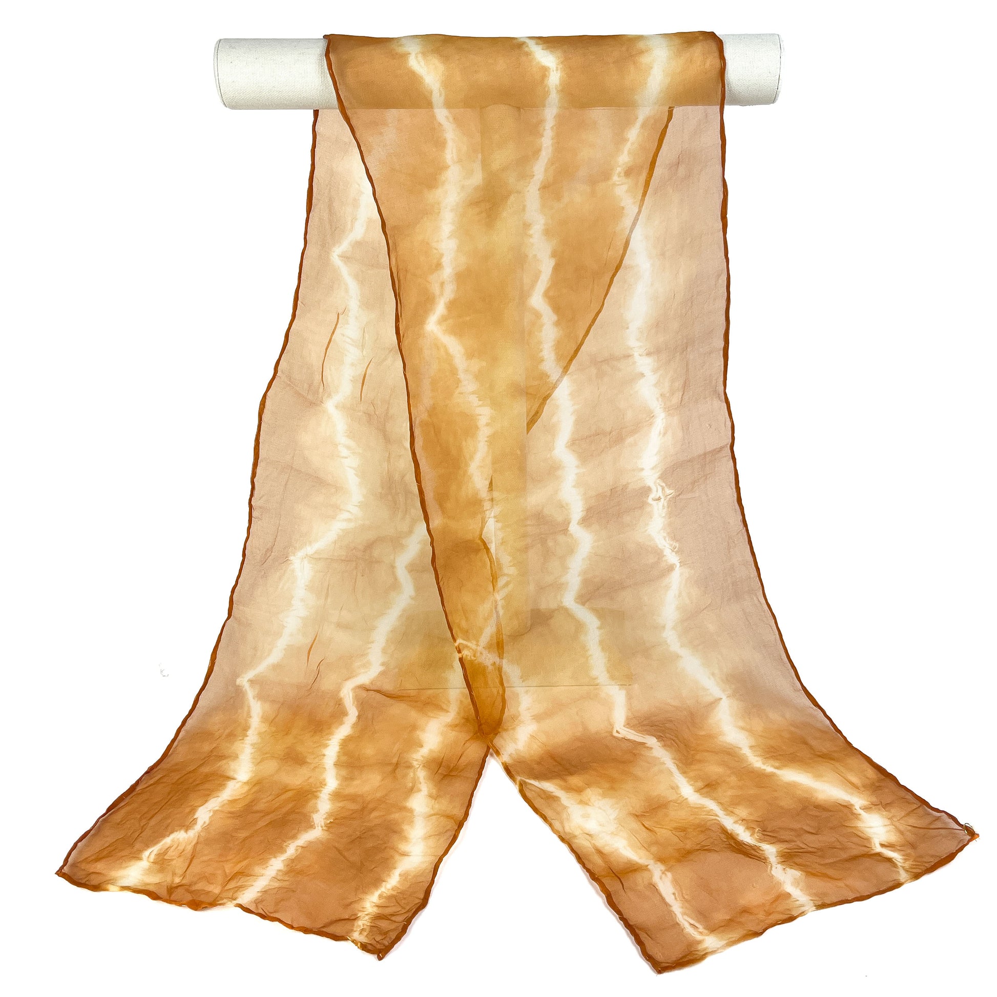 A Walnut Hull silk scarf with a wavy, horizontal shibori tie-dye pattern drapes from a white cylindrical bar.