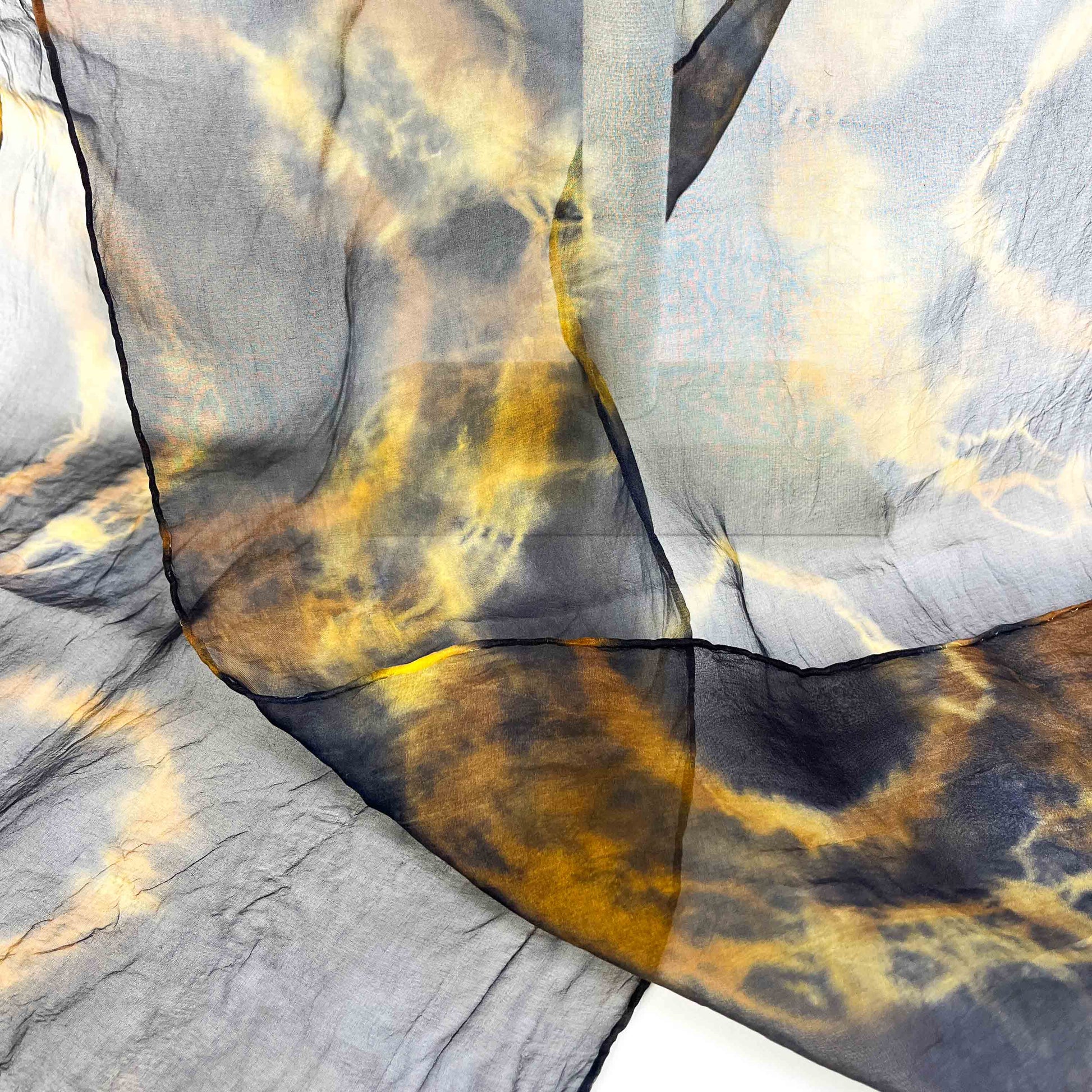 A close-up shows the delicate weave and swirling resist shibori pattern of a sheer silk scarf.