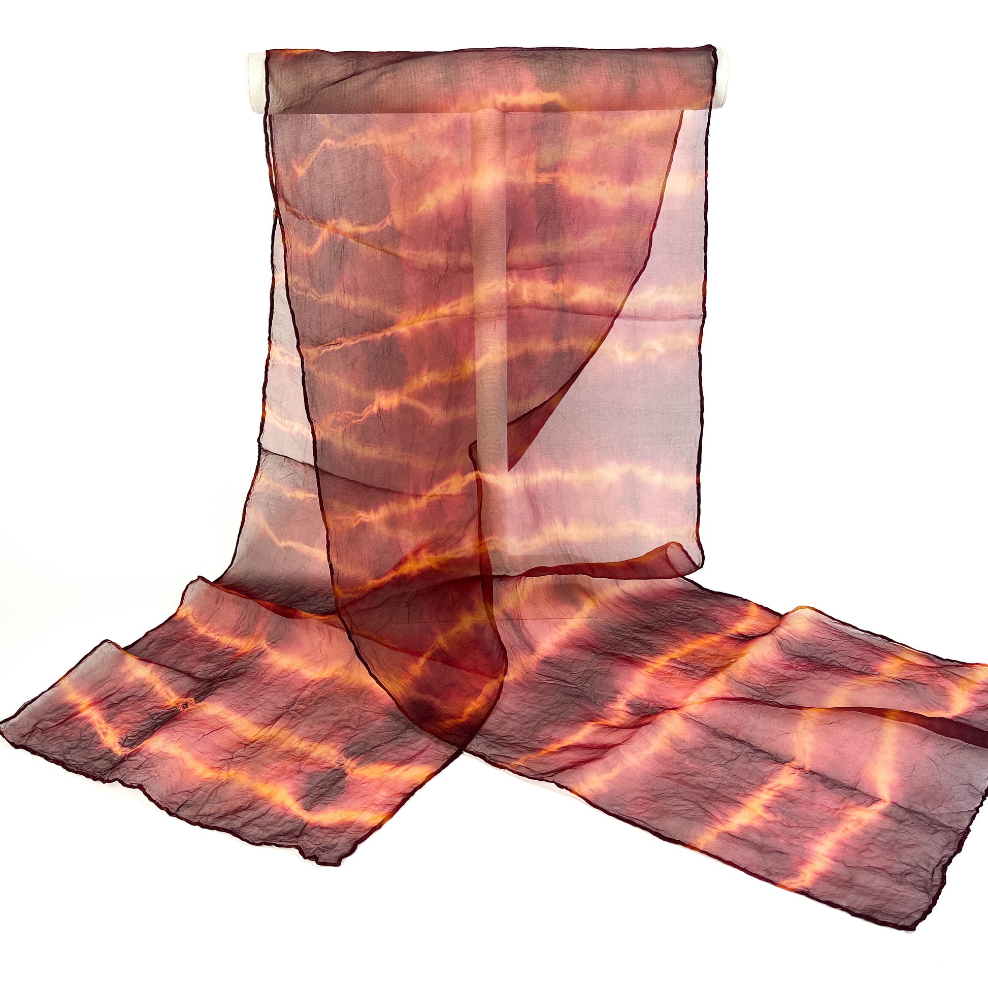 A sheer silk scarf with a horizontally striped and subtly textured tie-dye pattern hangs from a white cylindrical bar.