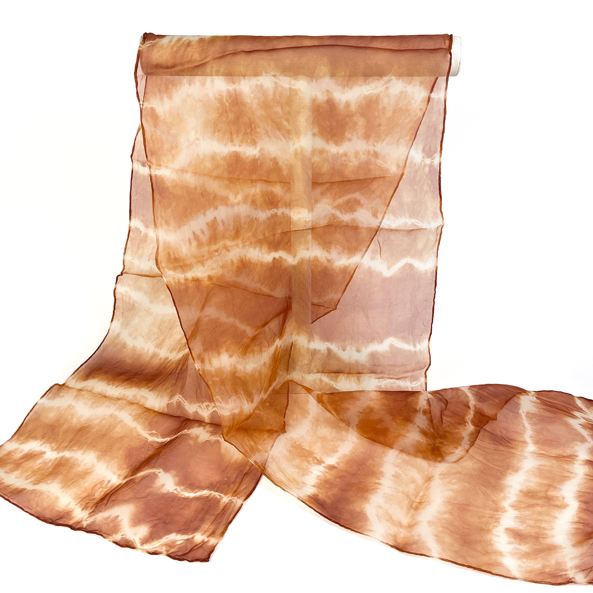 A sheer silk scarf with a horizontally textured and subtly blended tie-dye pattern hangs from a white cylindrical bar.