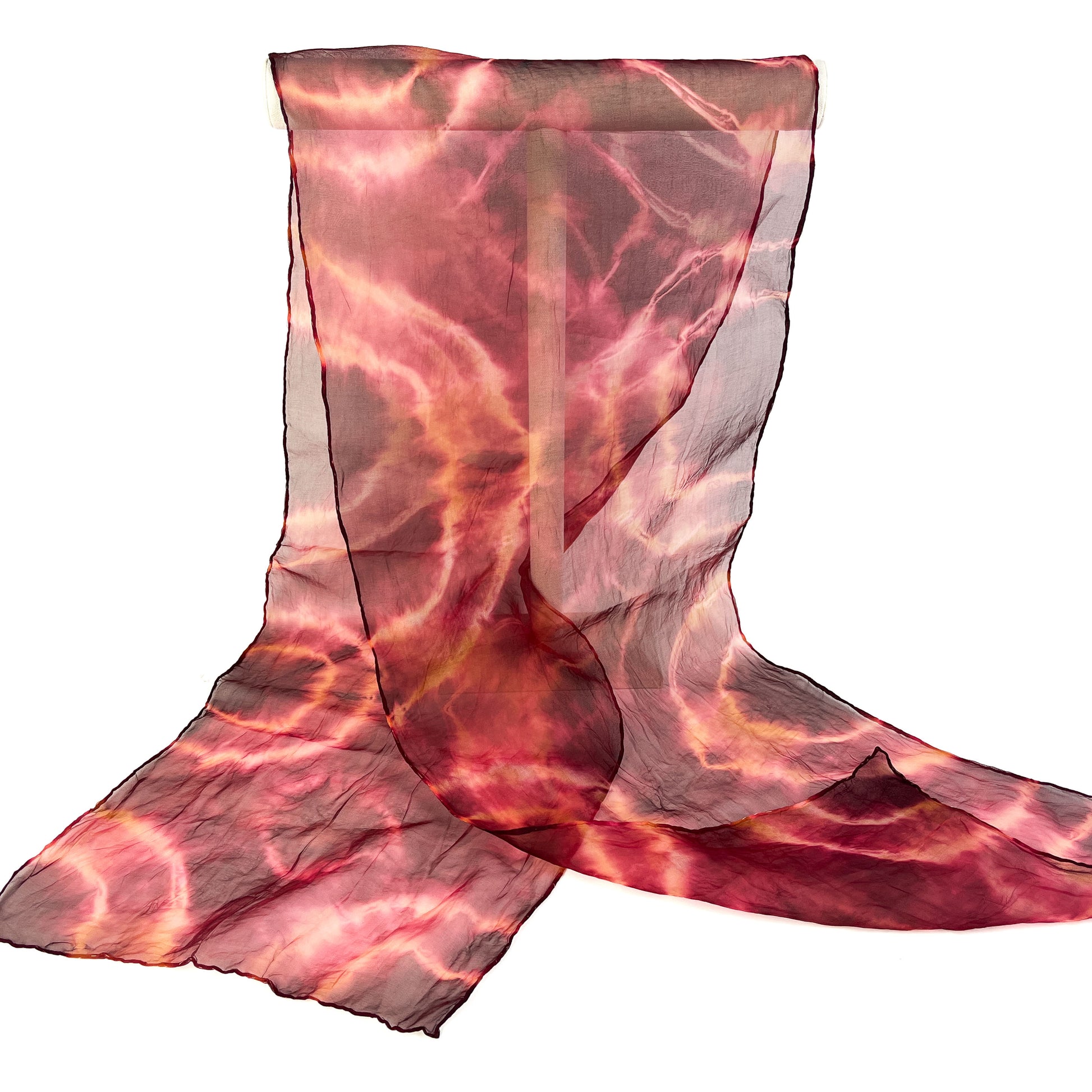 A sheer silk scarf with a vibrant, swirling tie-dye pattern in shades of red and orange is partially draped.