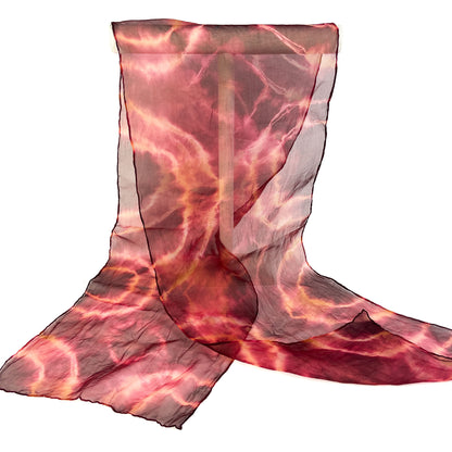 A sheer silk scarf with a vibrant, swirling tie-dye pattern in shades of red and orange is partially draped.