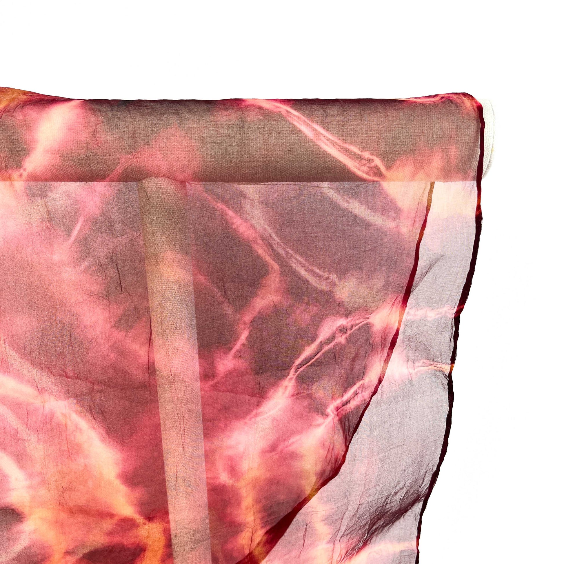 A close-up shows the delicate texture and swirling tie-dye pattern of a sheer silk scarf draped over a white bar.