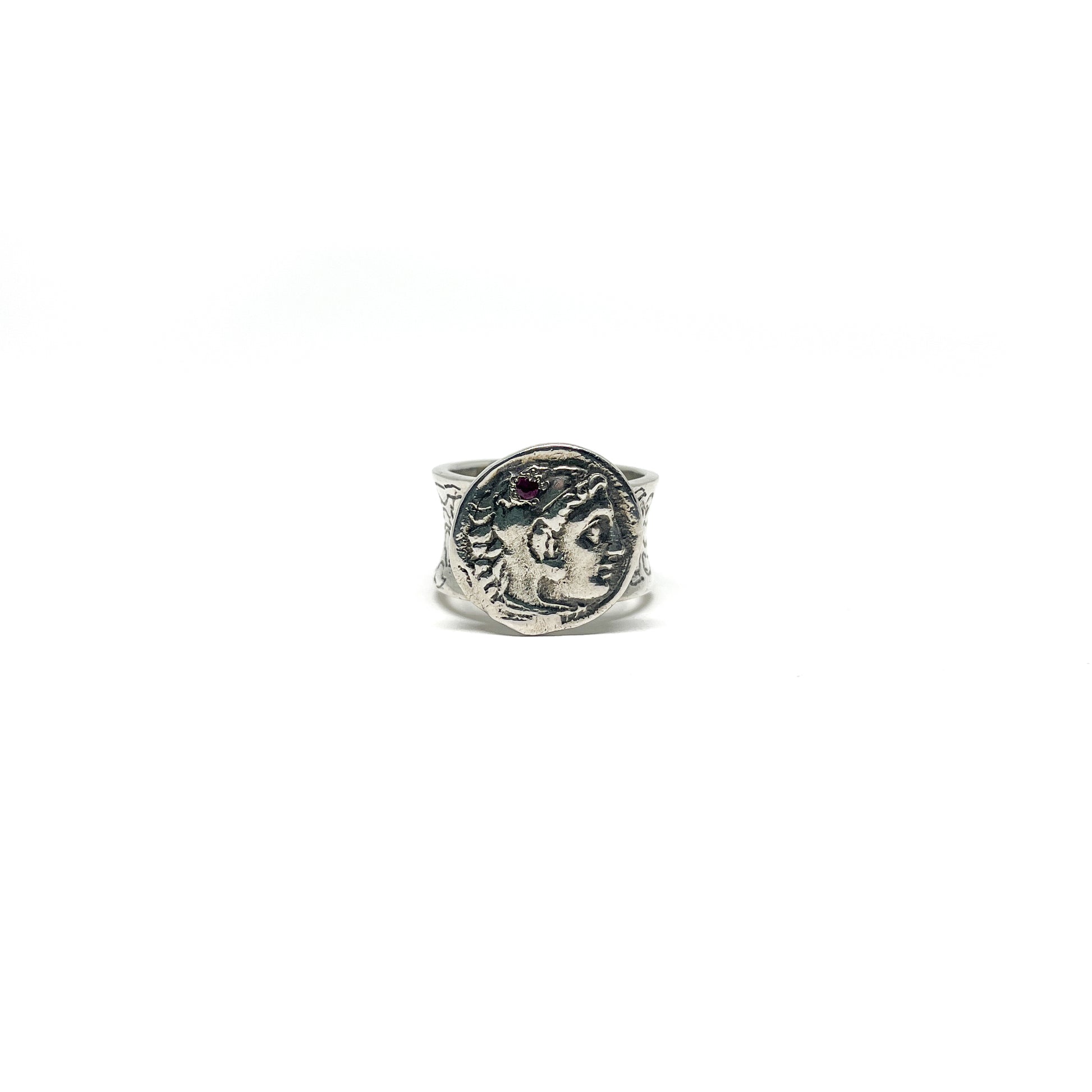 A detailed silver ring with an embedded antique coin showing two facing profiles and a decorative band with small red accents.