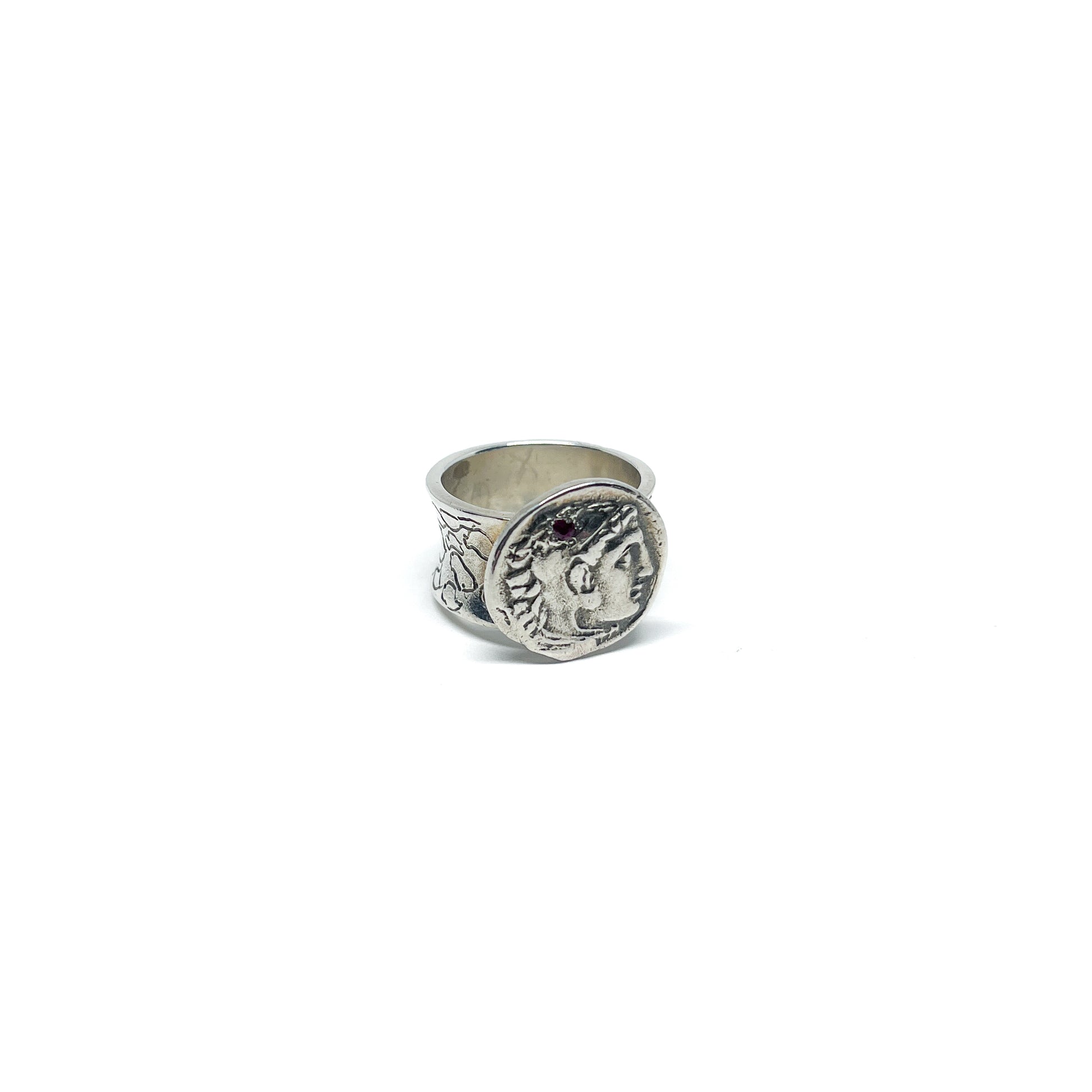 A silver ring featuring an antique coin with a profile of a person and a decorative band.