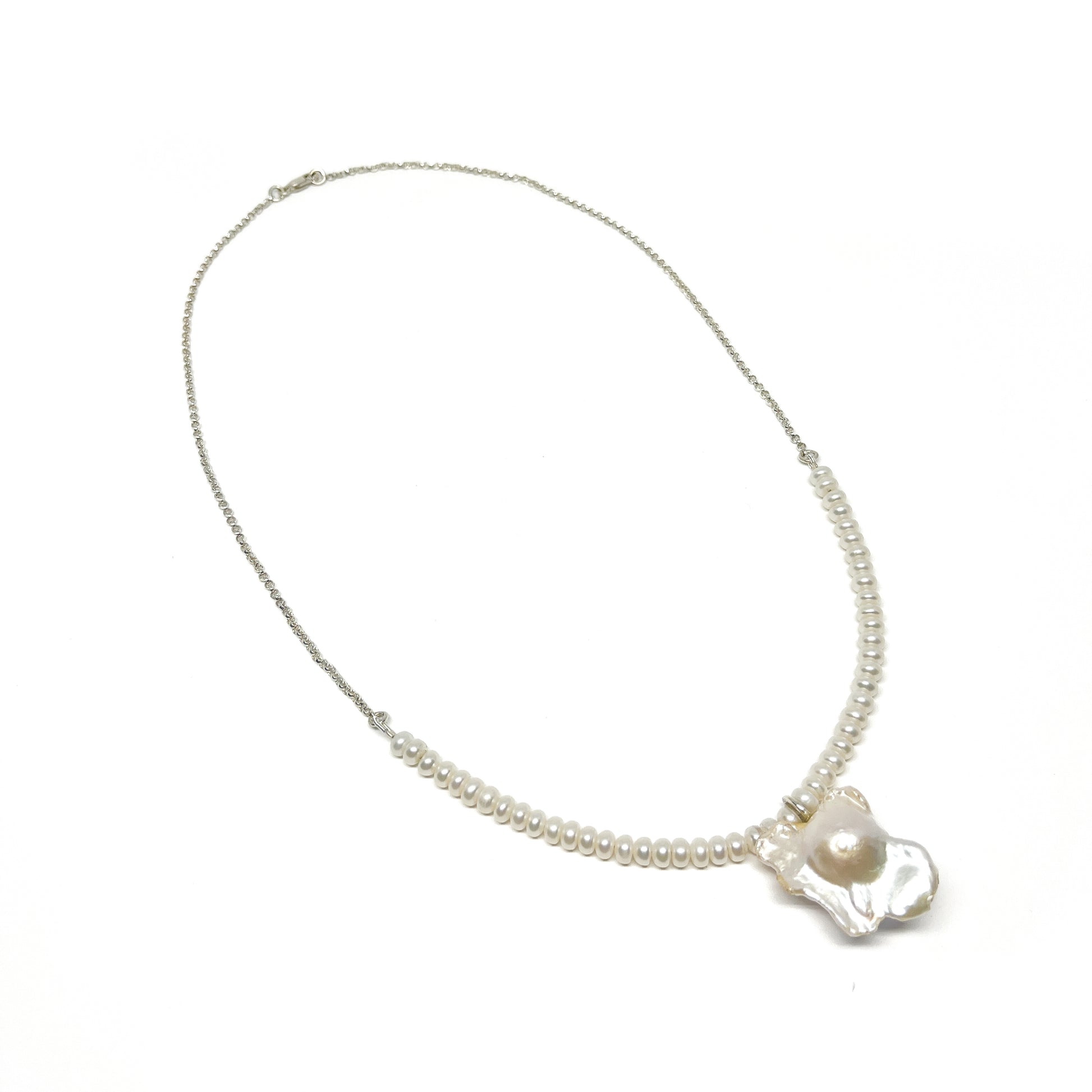 A pearl necklace with a chain on one side transitioning to small pearls, featuring a large, luminous baroque pearl pendant.