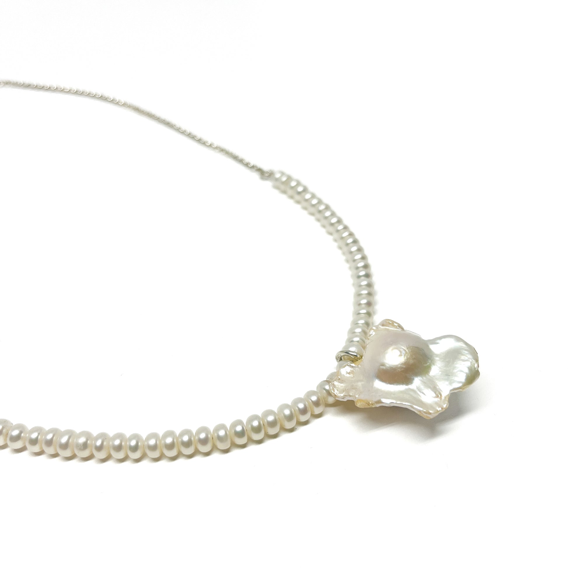 A delicate pearl necklace featuring small, round pearls and a larger, iridescent baroque pearl pendant.