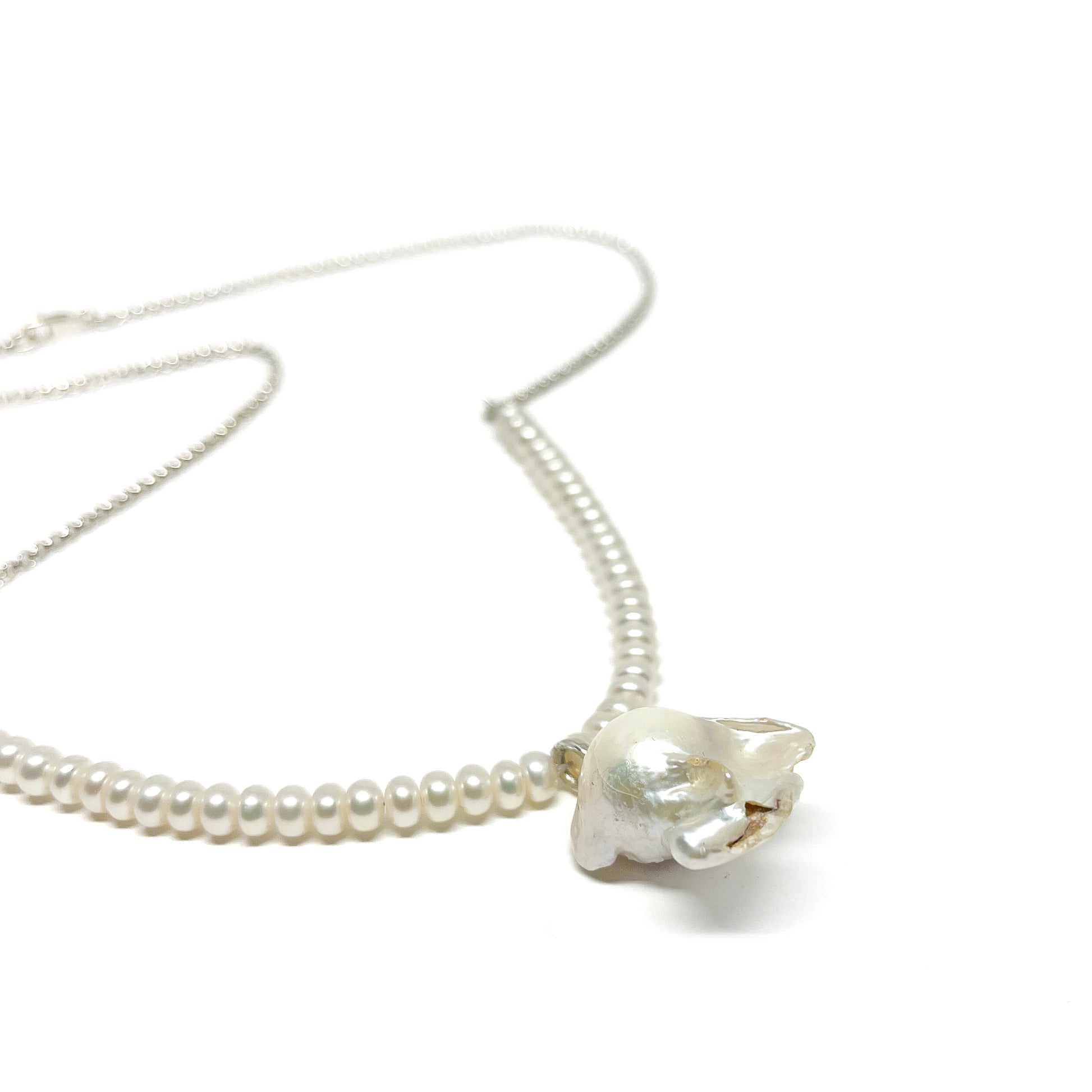Close-up of the Uverly White Natural Pearl Necklace featuring small round pearls and a uniquely shaped baroque pearl pendant.