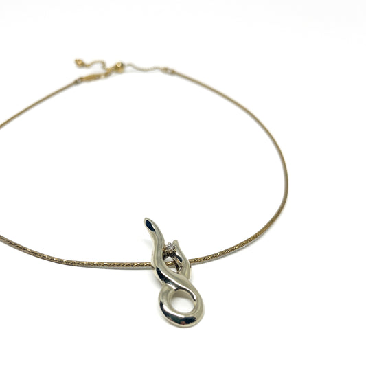 A delicate gold necklace featuring a polished silver abstract pendant with a small, sparkling stone.