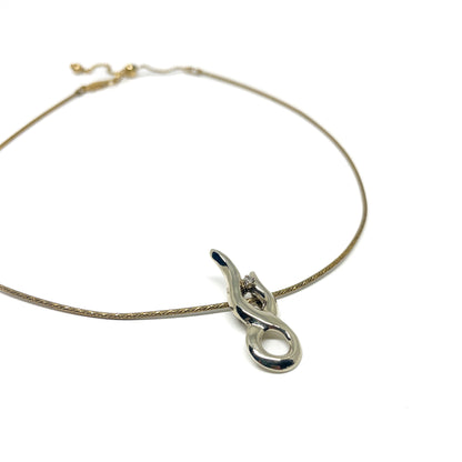A fine gold necklace featuring a sleek, polished silver abstract pendant with a small, brilliant gemstone.